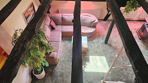 Un salón acogedor con un sofá rosa, una planta en maceta y una escalera.