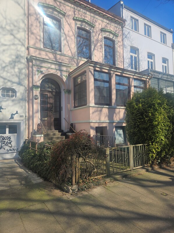 A two-story building with a large arched entrance, a small porch, and a gated front yard.