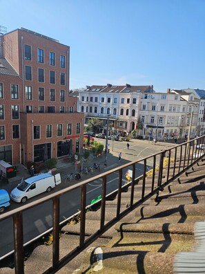 Ein mehrstöckiges Gebäude mit roten Backsteinfassaden und weißen Verkleidungen, eine Straße mit parkenden Autos und Fahrrädern sowie eine Fußgängerüberweg.