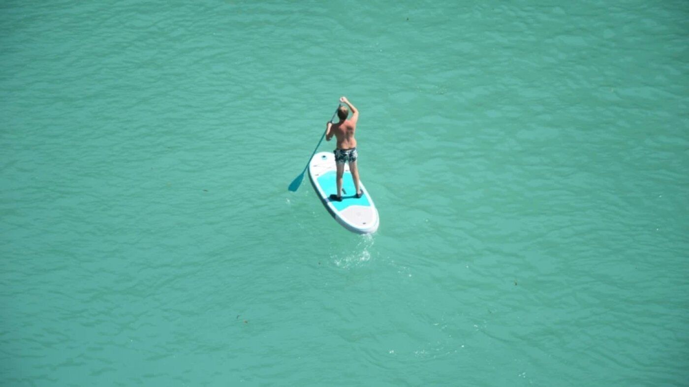 Eine Person steht auf einem Stand-Up-Paddleboard in klarem Wasser.