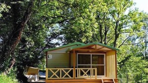 A small wooden cabin with a balcony, surrounded by trees.