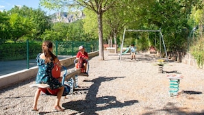 A playground with swings and a slide, surrounded by trees and a fence.