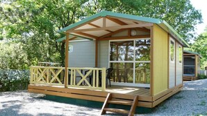 Une petite cabane dotée d’une terrasse en bois, d’un porche couvert et d’une façade avec des fenêtres.