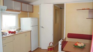 A compact kitchen with a refrigerator, sink, and a dining area with a table and bench.