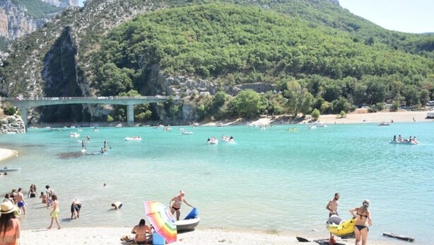 A beach with a bridge, boats, and people enjoying the water.