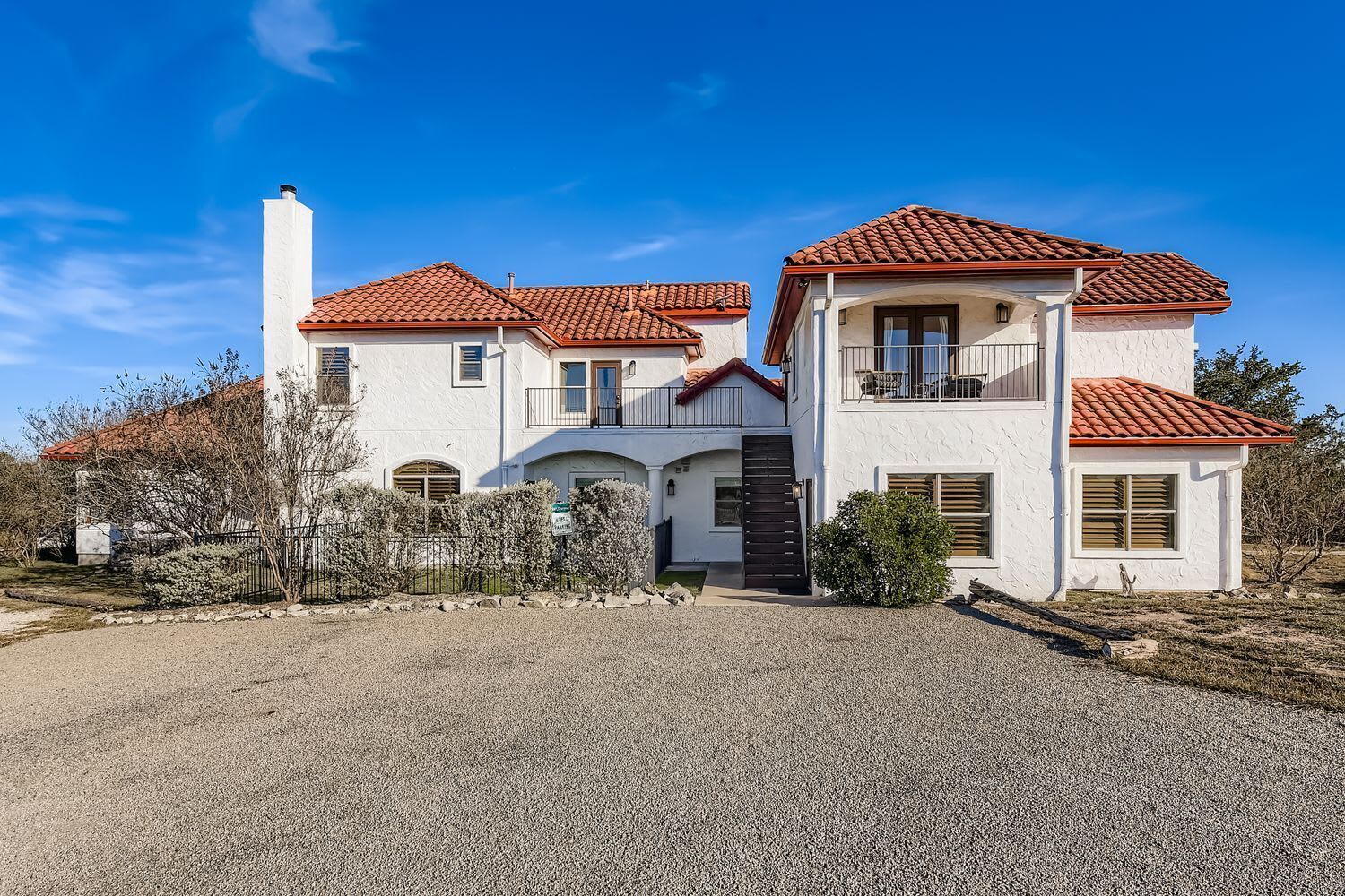 A two-story house with a red-tiled roof, white exterior walls, and a gravel driveway.