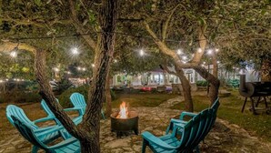 Un espacio al aire libre con sillas y una chimenea, rodeado de árboles y luces colgantes.