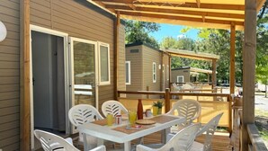 Un patio techado al aire libre con una mesa y sillas, una terraza de madera y vistas a otras cabañas.