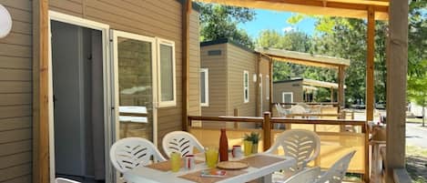 A covered outdoor patio with a table and chairs, a wooden deck, and a view of other cabins.