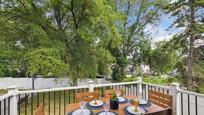 An outdoor dining area with a wooden table set for four, surrounded by a white railing. - Basketball Court, Pickleball, Karaoke, 6 Beds (Minneapolis)
