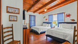 A room with two beds, wooden flooring, and nautical-themed decorations including sailboats and fish.