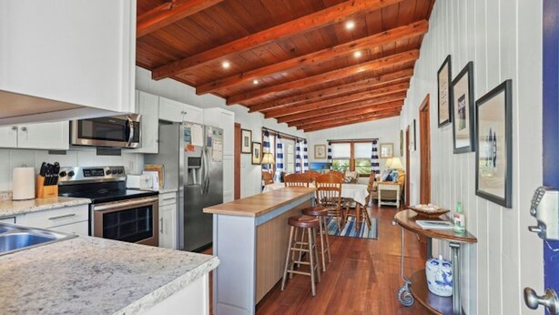 A spacious kitchen with a wooden ceiling, a central island with stools, and a dining area with a view.