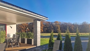 A covered patio area with outdoor furniture, a brick wall, and a view of a field and trees.