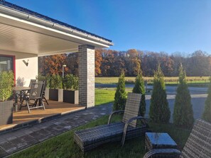 Ein überdachter Patio-Bereich mit Gartenmöbeln, einer Backsteinmauer und Blick auf ein Feld und Bäume.
