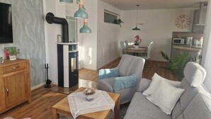A modern living room with a sofa, a coffee table, and a TV. There is a kitchen area with a microwave and a dining table.