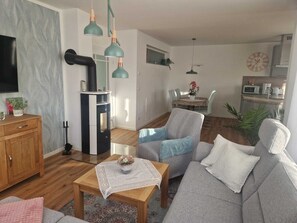 Ein modernes Wohnzimmer mit einer Couch, einem Couchtisch und einem Fernseher. Es gibt eine Küchenzeile mit einer Mikrowelle und einem Esstisch.