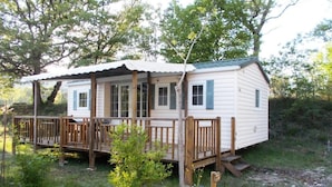 A small, single-story cabin with a porch and wooden railings, surrounded by trees.