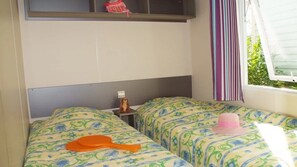 A room with two beds, each with patterned bedding, a small table with a figurine, and a window with curtains.