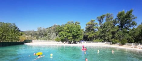 Una piscina azul cristalina rodeada de árboles y una playa de arena.