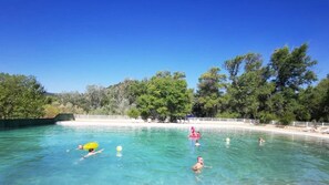 A clear blue pool surrounded by trees and a sandy beach.