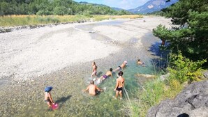 A group of people swimming in a river surrounded by greenery and mountains.