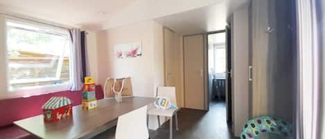A room with a dining table, chairs, a window with curtains, a door, and a small play area with a colorful toy.