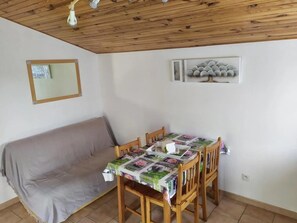 Un área de comedor con una mesa y sillas de madera, un sofá gris y un techo con vigas de madera.