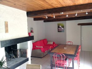 A cozy room with a wooden ceiling, a fireplace, a red sofa, a dining table with chairs, and a wall-mounted light fixture.
