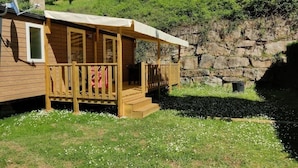 A wooden cabin with a porch, a small window, and a stone wall in the background. - ZEcamping 4* piscine animations locatif TV clim 32m2 4 pers (Saint-Rome-de-Tarn)