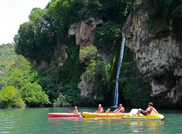 A group of people kayaking on a calm river with a waterfall in the background.
