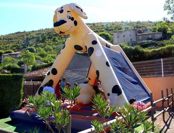 A large inflatable dog slide with a smiling face, surrounded by greenery and a fence. - ZEcamping 4* piscine animations locatif TV clim 32m2 4 pers (Saint-Rome-de-Tarn)