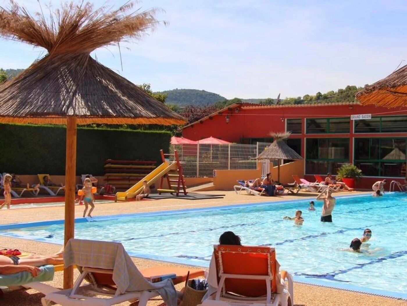 A swimming pool area with lounge chairs, a slide, and a building labeled "GRAND BASIN".