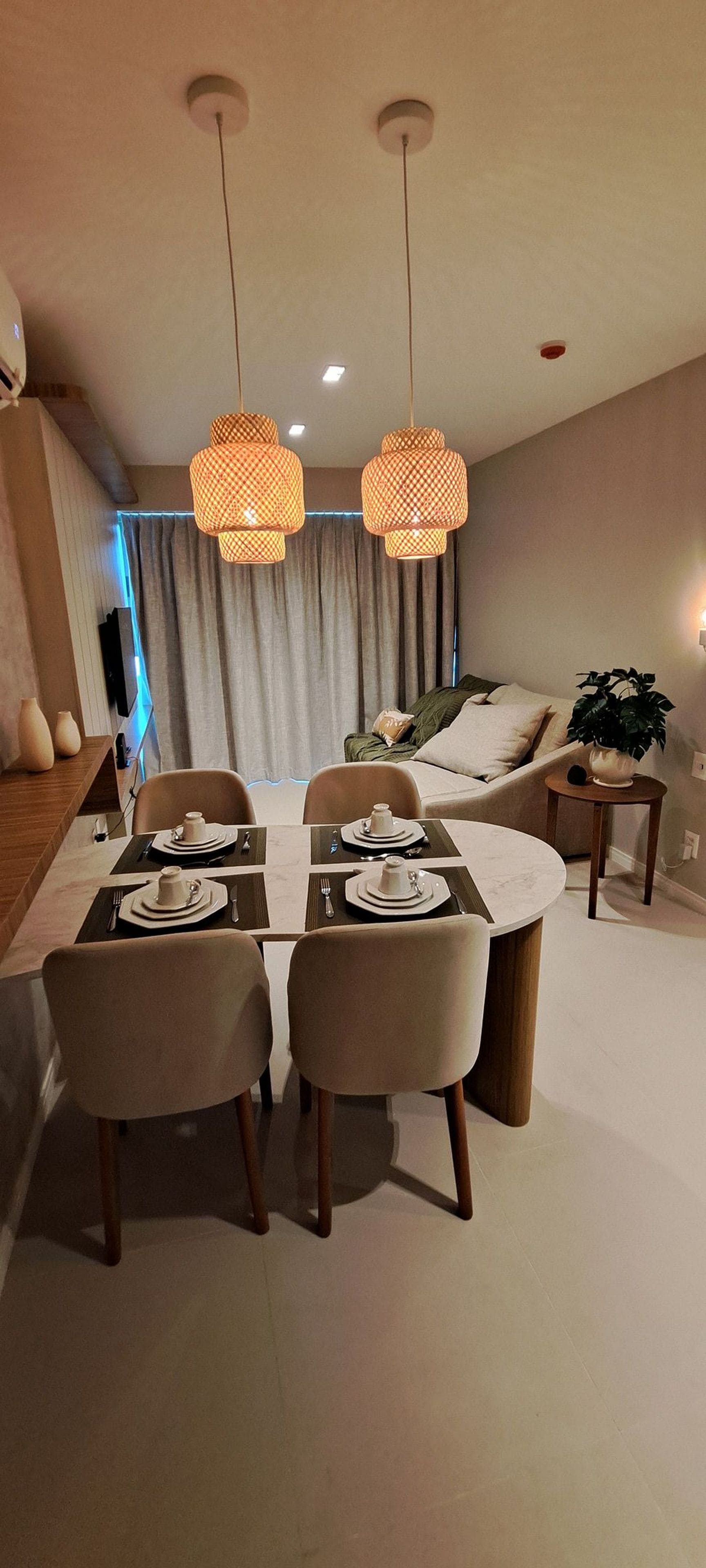 A modern dining area with a round table set for four, two pendant lights, and a sofa in the background.