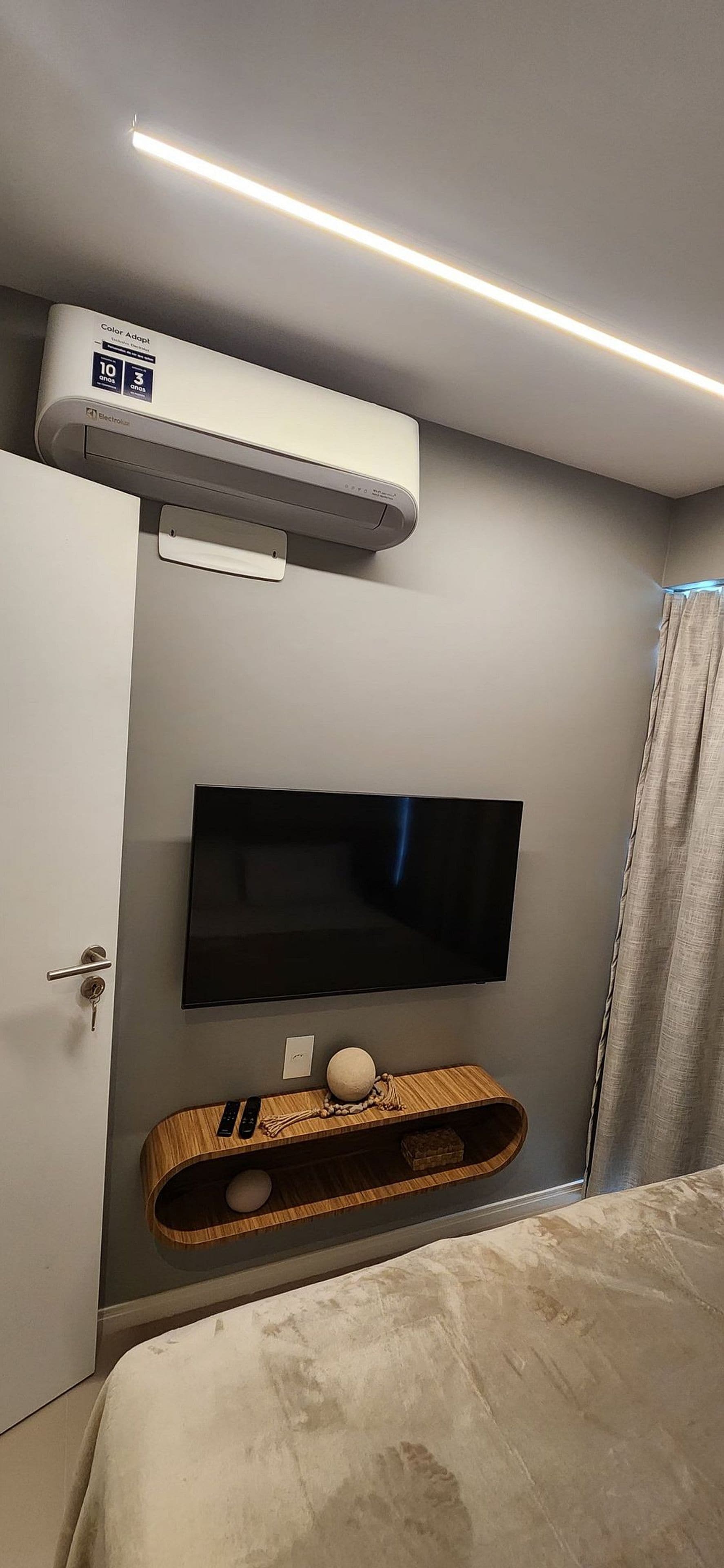 A bedroom with a flat-screen TV mounted on the wall, a wooden console table with a remote and a decorative item, and an air conditioning unit above the door.