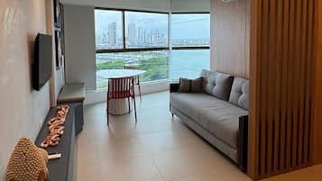 A modern living room with a sofa, a dining table, and a view of a cityscape through large windows.