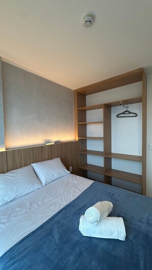 A hotel room with a bed, a headboard, a wall-mounted shelf, and a hanging coat rack. - Flats no Parque do Cais Recife  (Recife)