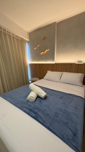 Ett hotellrum med en säng, gardiner, ett nattduksbord och en vägg med en lampa.
