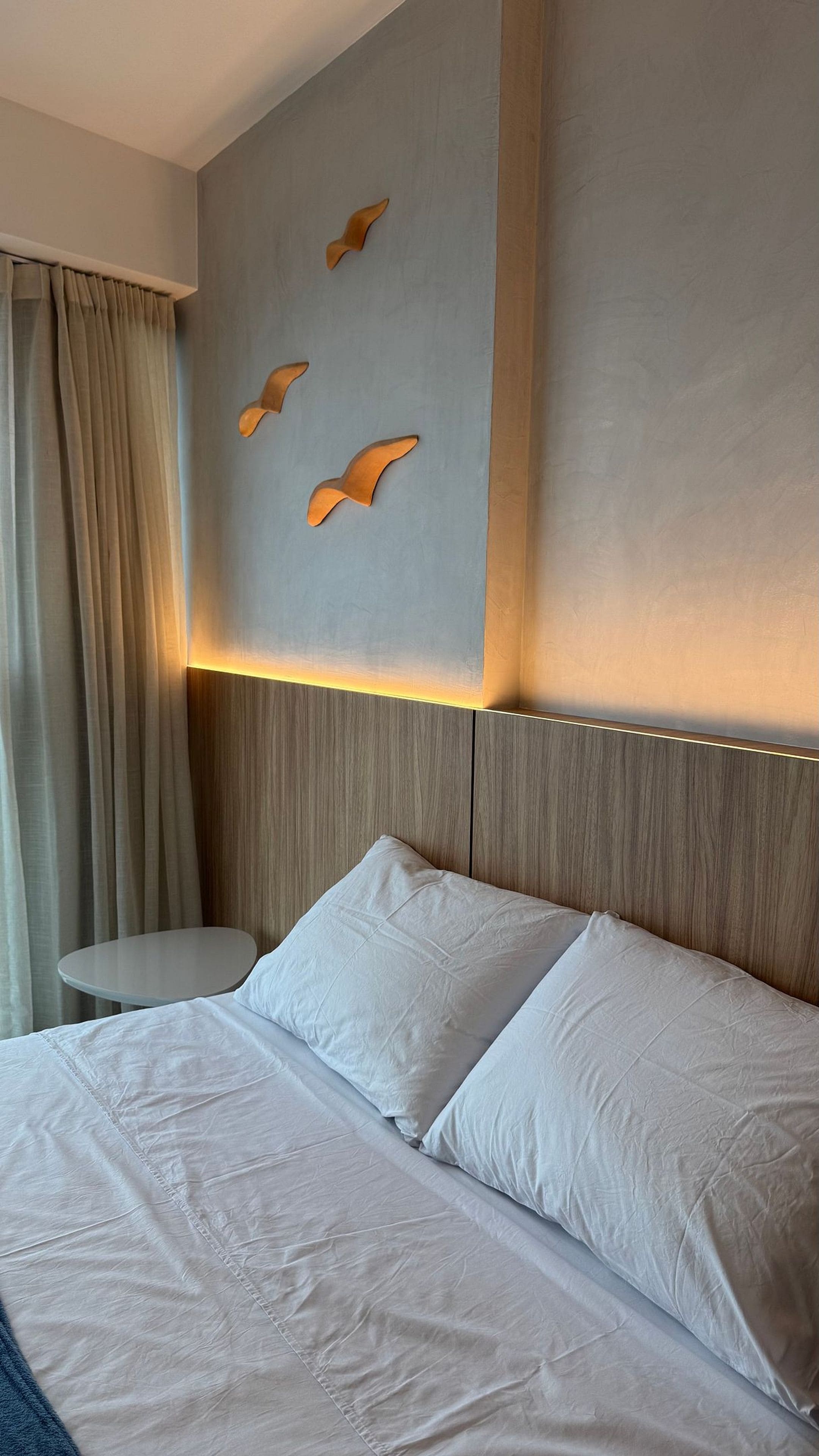 Habitación de hotel con una cama grande, una mesita redonda y una pared con revestimiento de madera clara y detalles decorativos.