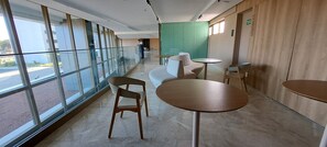 A modern interior with large windows, a seating area with tables, and a green partition wall. - Flats no Parque do Cais Recife  (Recife)