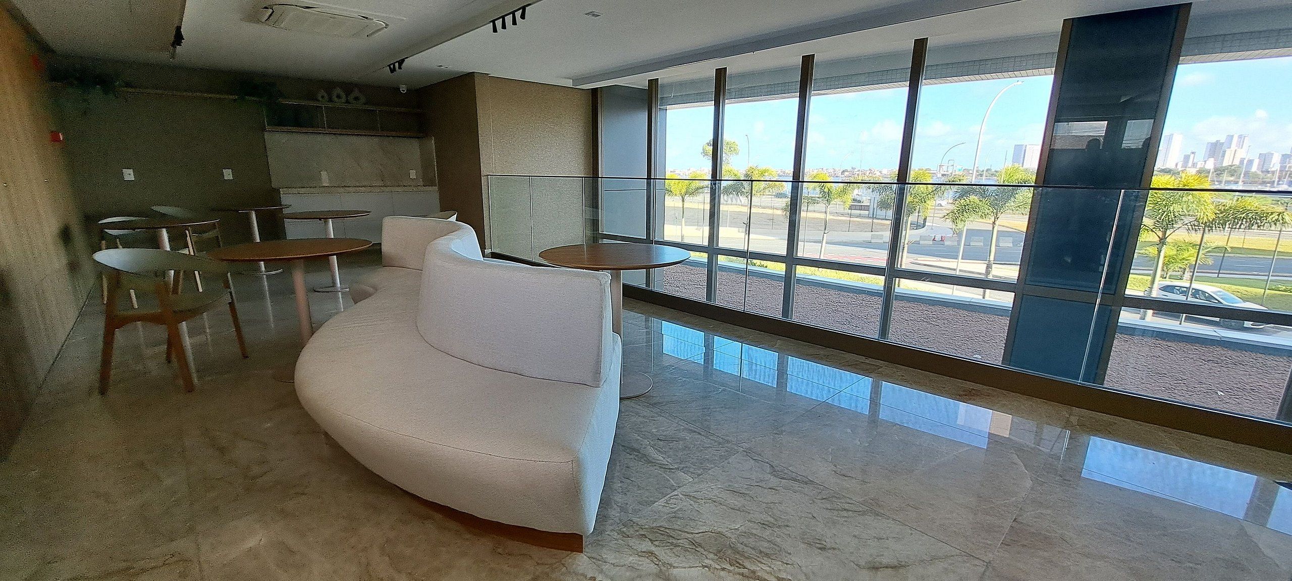 Un lobby moderno con un sofá blanco curvo, mesas redondas y un amplio ventanal con vistas a la ciudad.