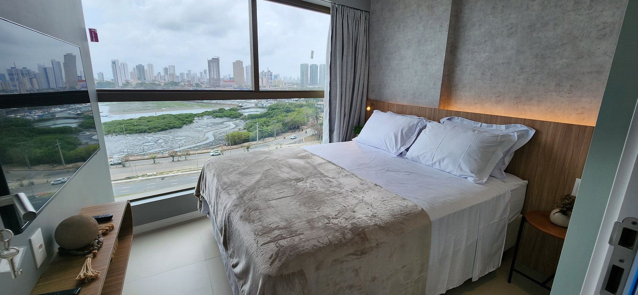 Habitación de hotel moderna con una cama grande, cabecera de madera y vistas a la ciudad y al río.