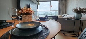A modern dining area with a city view, a sofa, and a table set with plates, bowls, and wine glasses. - Flats no Parque do Cais Recife (Recife)