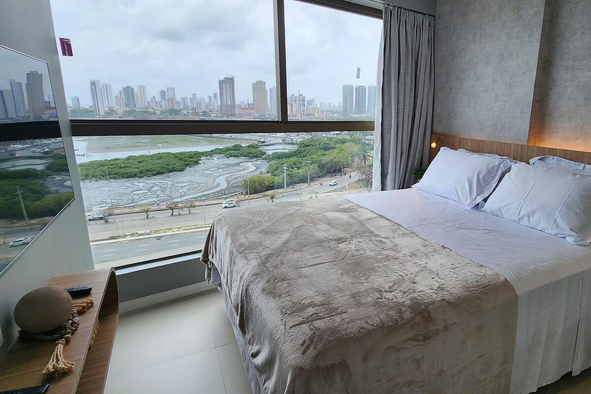 Habitación de hotel moderna con una cama grande, cabecera de madera y vistas a la ciudad y al río.