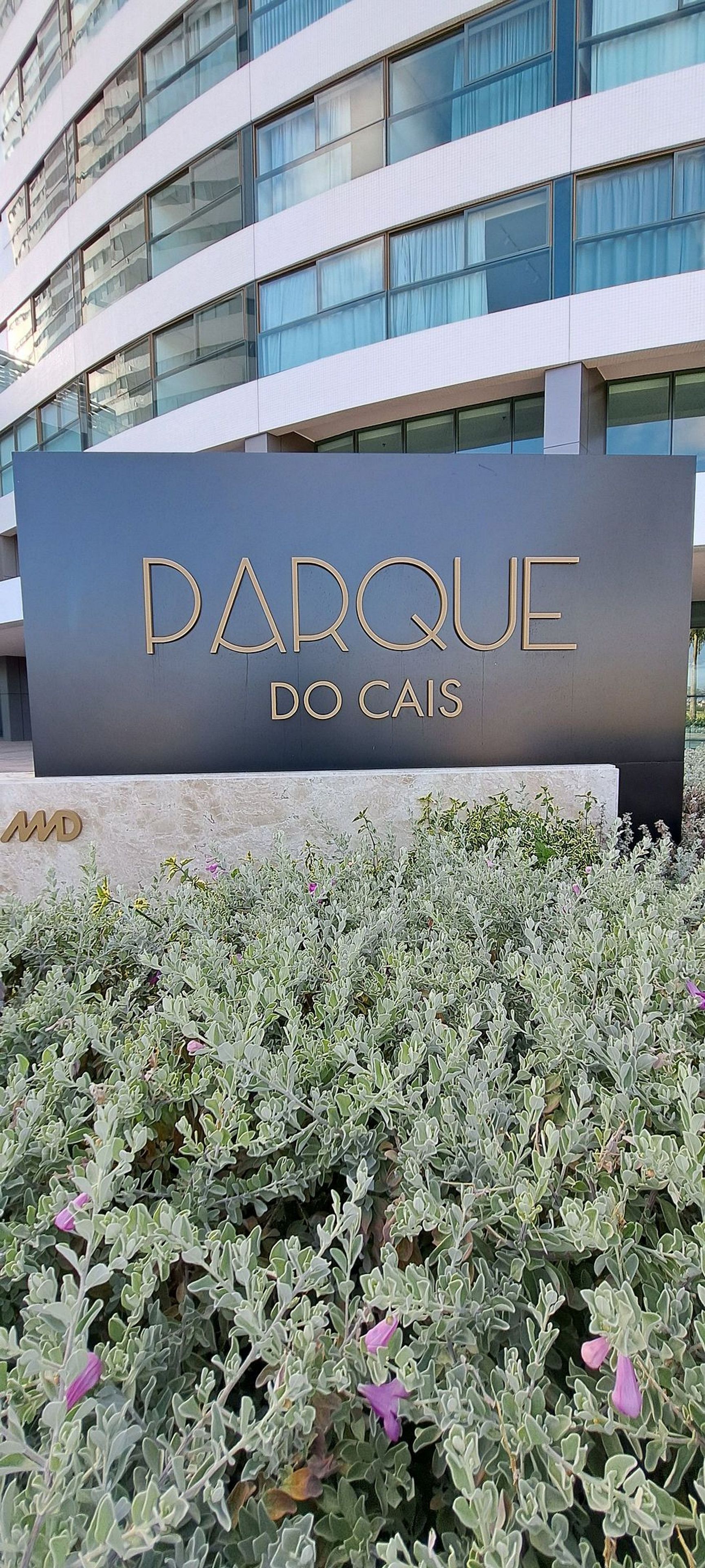 Señalización para 'PARQUE DO CAIS' con un edificio moderno al fondo.