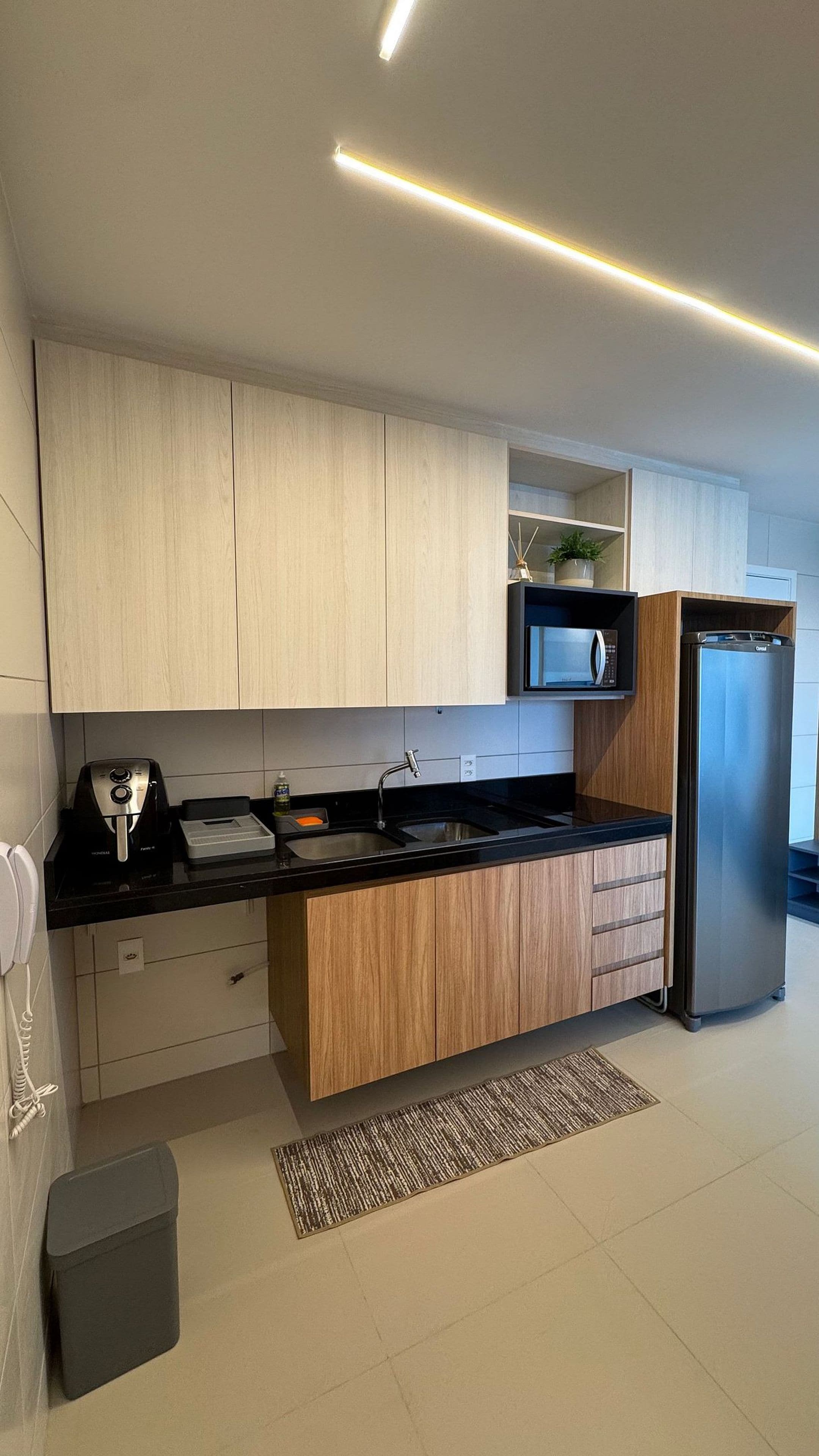 A modern kitchen with wooden cabinets, a black countertop, a built-in microwave, and a stainless steel refrigerator.