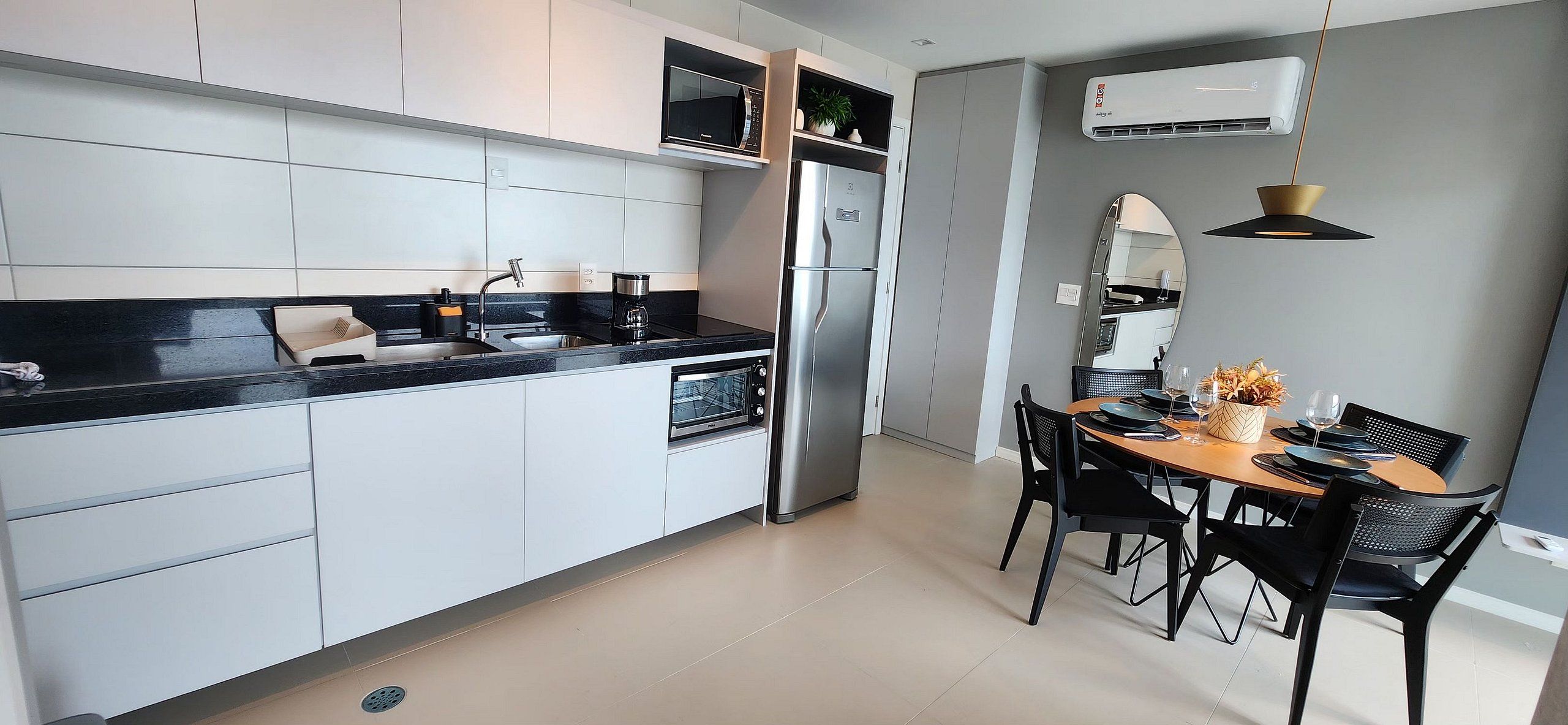 Una cocina moderna con armarios blancos, encimera negra, refrigerador de acero inoxidable y un comedor con mesa de madera y sillas negras.