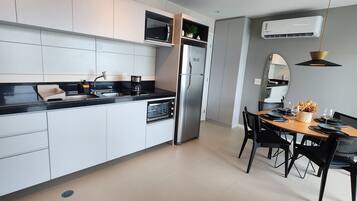Una cocina moderna con armarios blancos, encimera negra, refrigerador de acero inoxidable y un comedor con mesa de madera y sillas negras.