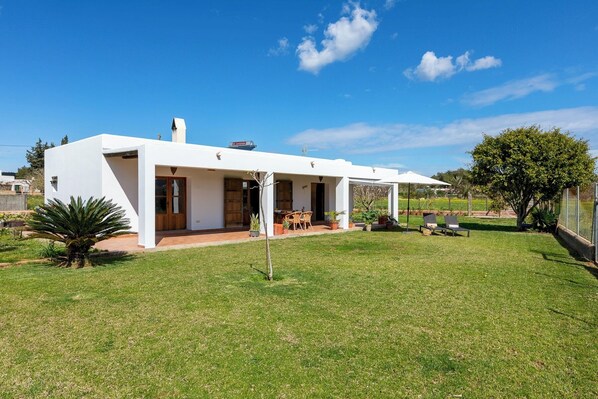Una casa blanca moderna con un patio, un pequeño jardín y un cielo azul despejado.