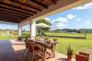 Un patio exterior con una mesa de madera, sillas de mimbre y un paraguas blanco.