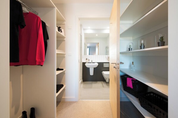 A modern bathroom with a white sink, toilet, and a mirror above the sink. There are shelves on either side of the door, and a pair of black shoes on the floor. - Duet - Campus Accommodation (Salford)